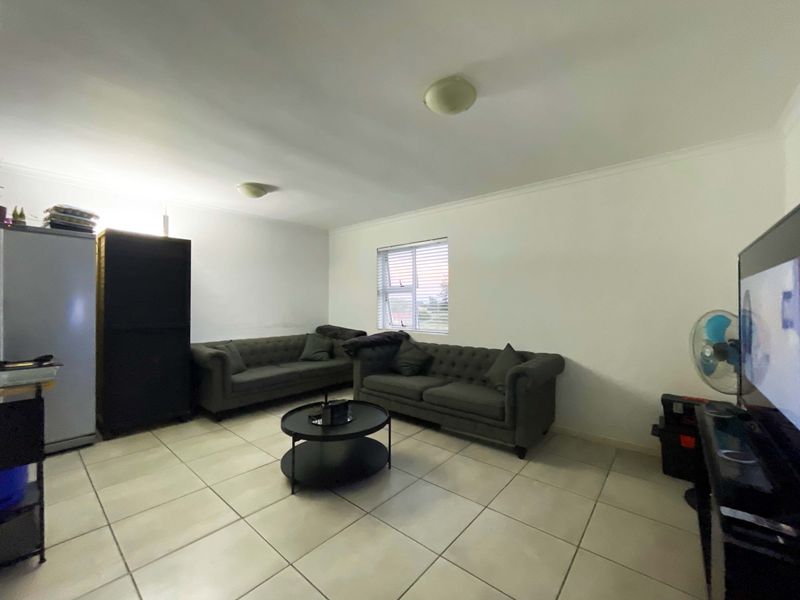 A functional living room featuring neutral tiled flooring, white walls with cove cornicing, and a window fitted with horizontal blinds.