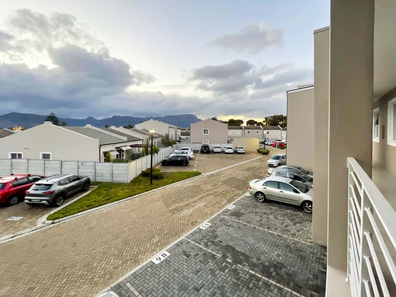 Elevated view of the apartment complex parking area, featuring paved driveways, designated parking bays, and surrounding residential units with mountain views.