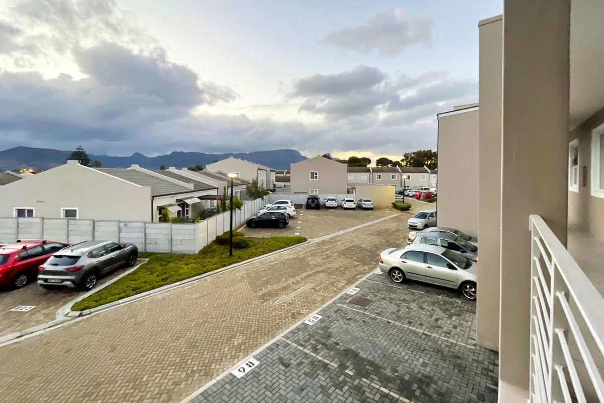 Elevated view of the apartment complex parking area, featuring paved driveways, designated parking bays, and surrounding residential units with mountain views.