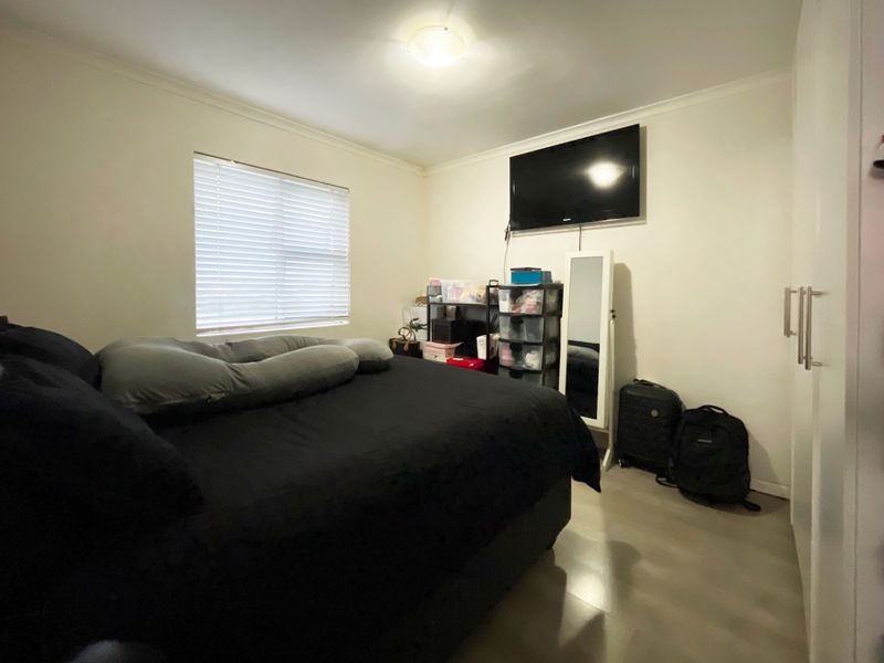 A functional bedroom featuring laminate flooring, a built-in wardrobe, and venetian blinds, providing a neutral base for potential interior updates.