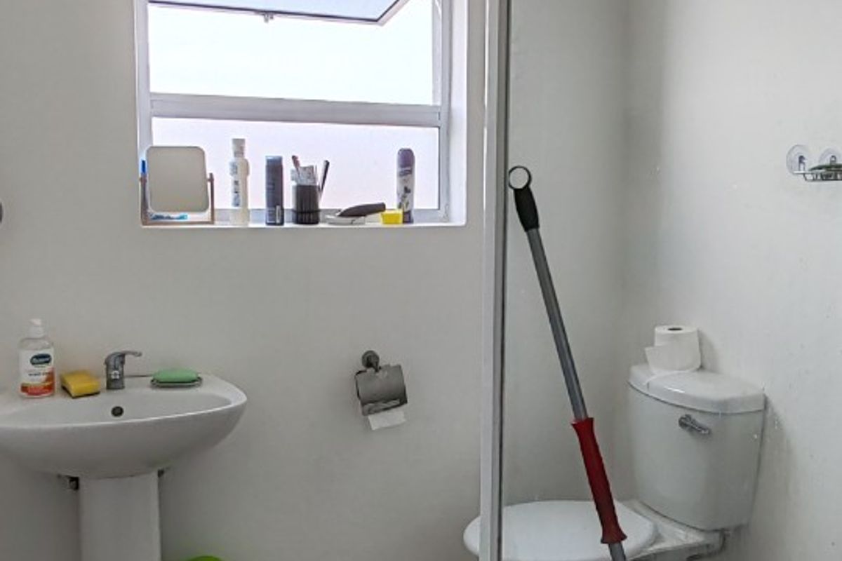 A functional bathroom featuring a pedestal basin, toilet, and a glass-enclosed shower with tiled flooring and natural light from a window.