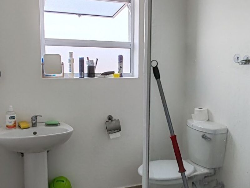 A functional bathroom featuring a pedestal basin, toilet, and a glass-enclosed shower with tiled flooring and natural light from a window.