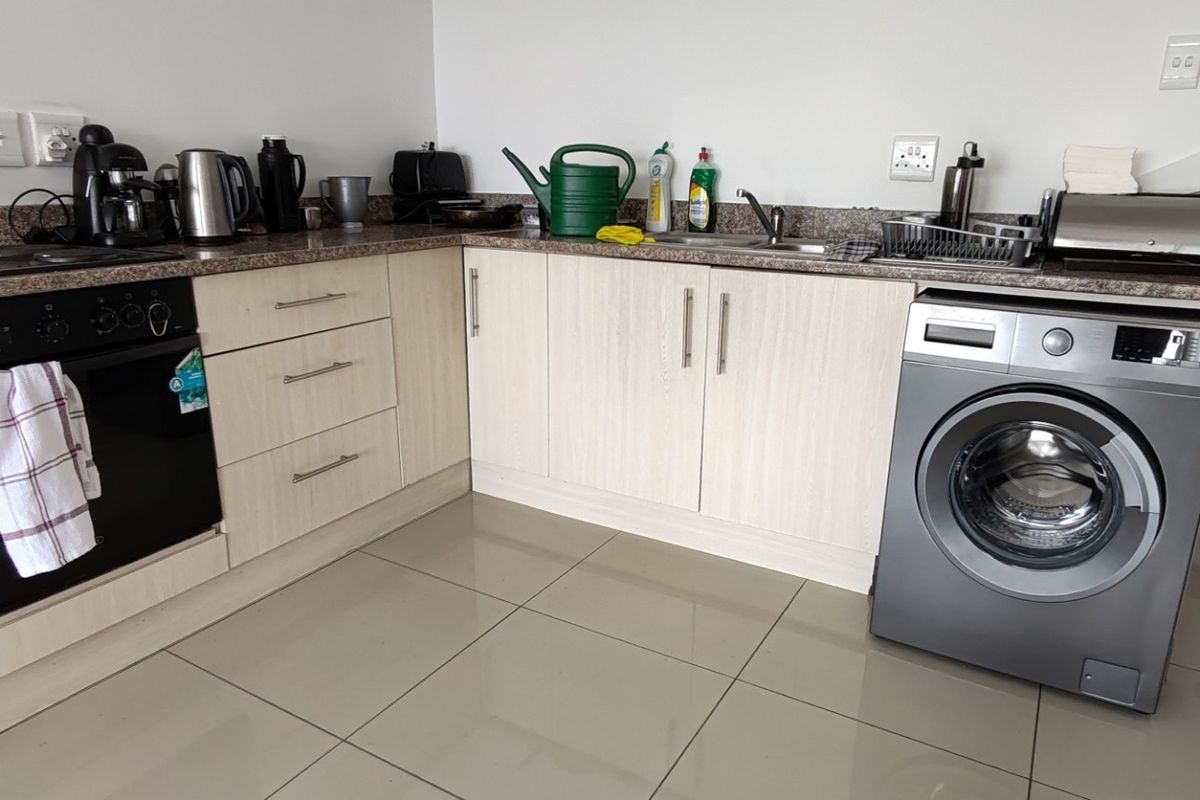 A functional kitchen featuring light wood-finish cabinetry, granite countertops, a built-in oven, and a dedicated space for a washing machine with tiled flooring.