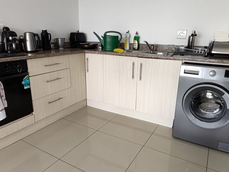 A functional kitchen featuring light wood-finish cabinetry, granite countertops, a built-in oven, and a dedicated space for a washing machine with tiled flooring.