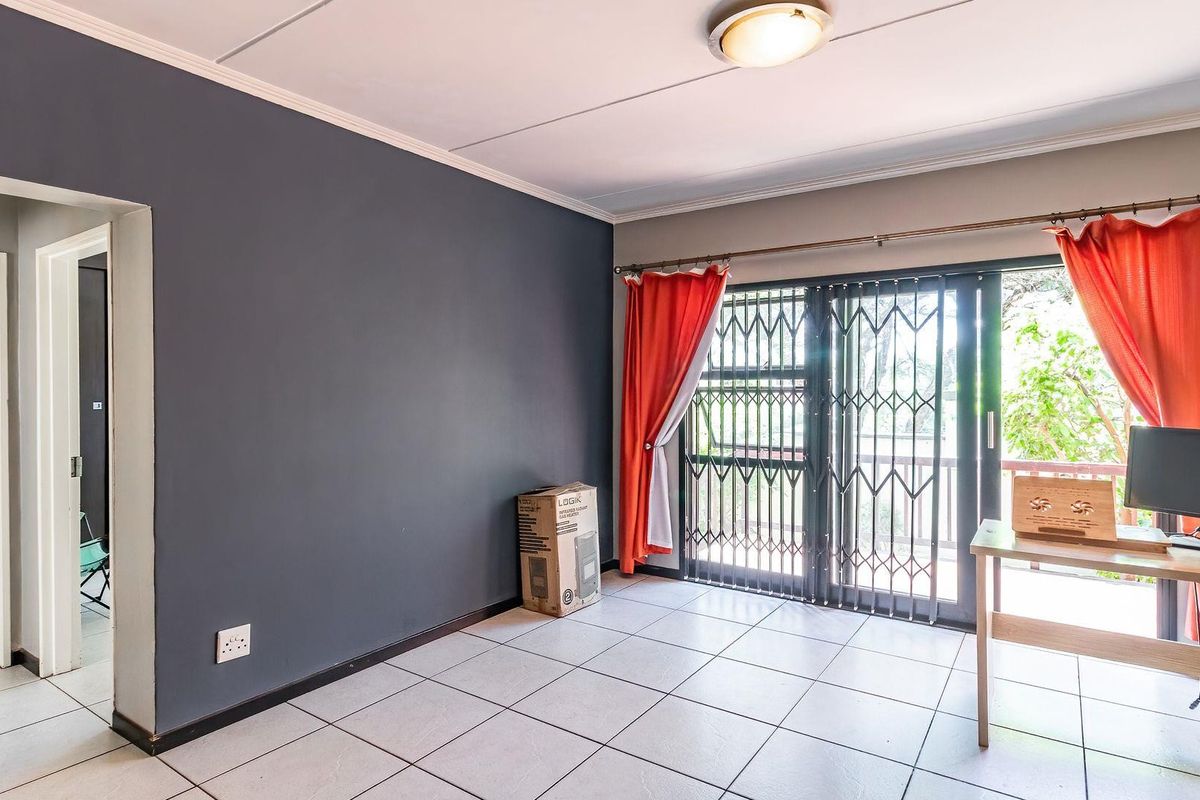 A living room featuring tiled flooring, a dark accent wall, and a sliding glass door with a security gate leading to an outdoor area.