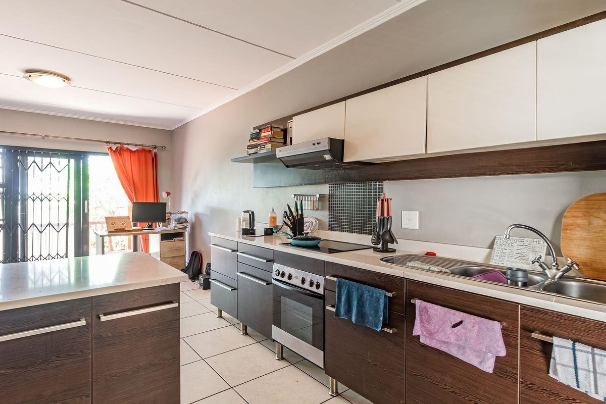 A functional kitchen featuring dark wood-finish cabinetry, a built-in oven and stove, extractor fan, and tiled flooring, with an adjacent open-plan living area.