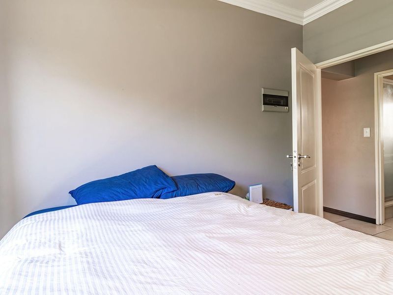 A bedroom featuring neutral wall tones, crown molding, and an integrated electrical distribution board, with an adjacent doorway leading to an adjoining space.