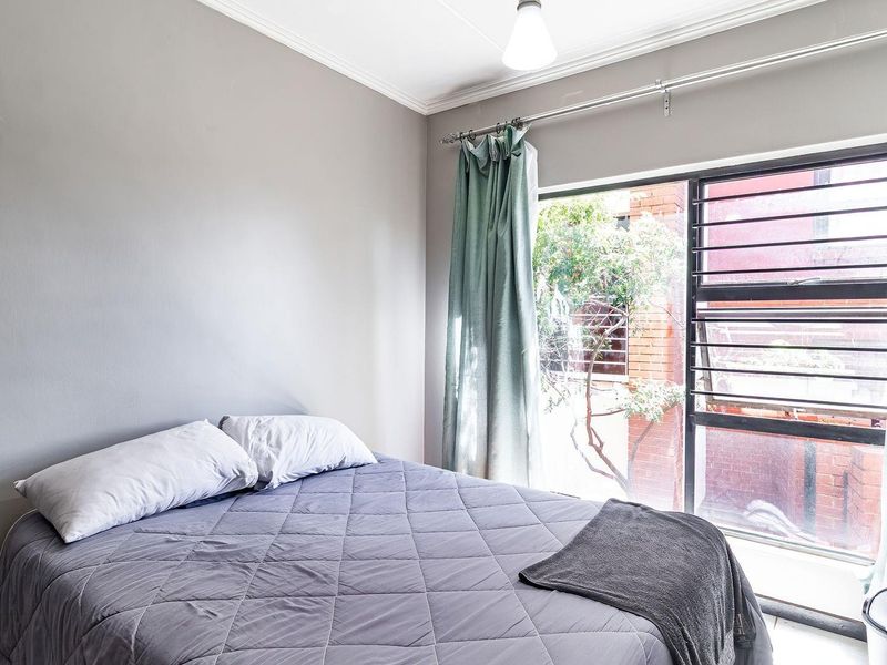 A bedroom featuring a louvered window with security bars, neutral grey walls, and decorative cove cornicing.