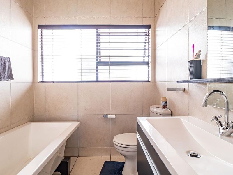 A functional bathroom featuring a bathtub, toilet, and vanity basin with neutral wall and floor tiling.