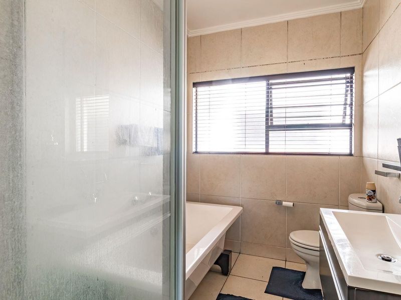 A functional bathroom featuring a shower enclosure, bathtub, toilet, and vanity basin with neutral wall and floor tiling.