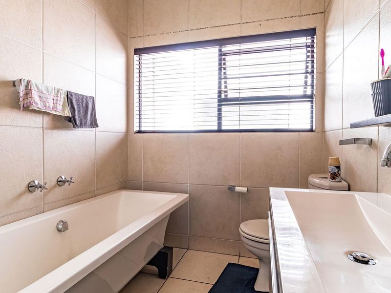 A functional bathroom featuring a freestanding bathtub, wall-mounted fixtures, a vanity basin, and neutral floor-to-ceiling wall tiling.