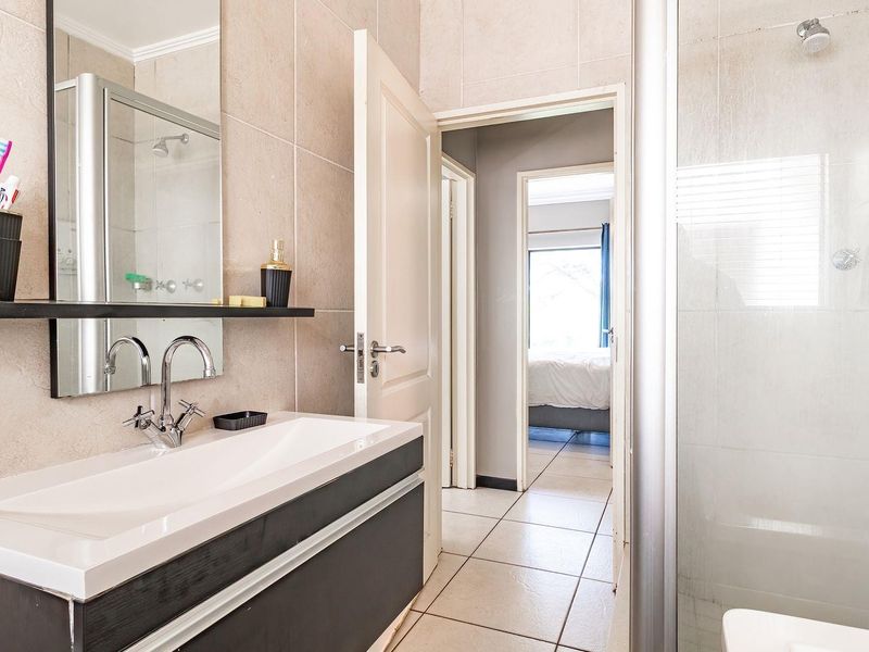 A modern bathroom featuring a vanity with basin, wall-mounted mirror, and a glass-enclosed shower with tiled walls and flooring.