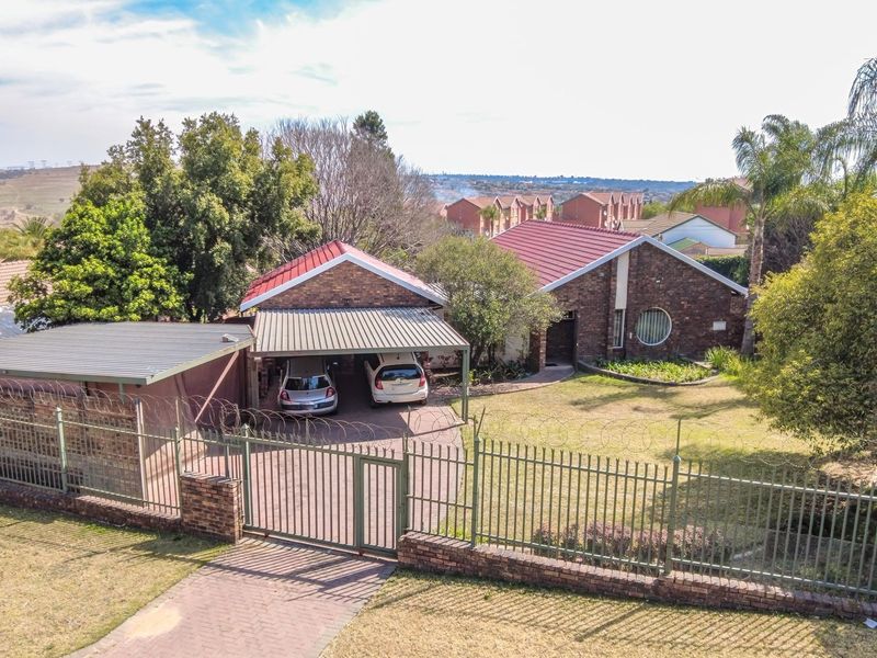 Aerial view of a brick house featuring a metal roof, carport, paved driveway, and secure perimeter fencing with razor wire.