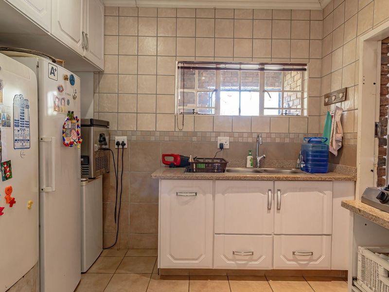 A functional kitchen area featuring white cabinetry, granite countertops, a double sink, and tiled splashbacks with a window providing natural light.