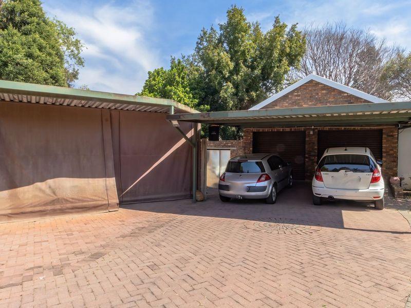 A functional double garage with a paved driveway and an attached carport featuring protective side screens.