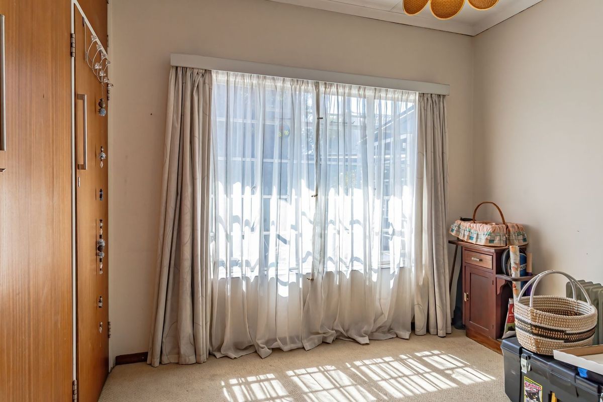 A bedroom featuring a built-in wooden wardrobe and a large window with curtains, providing natural light to the space.