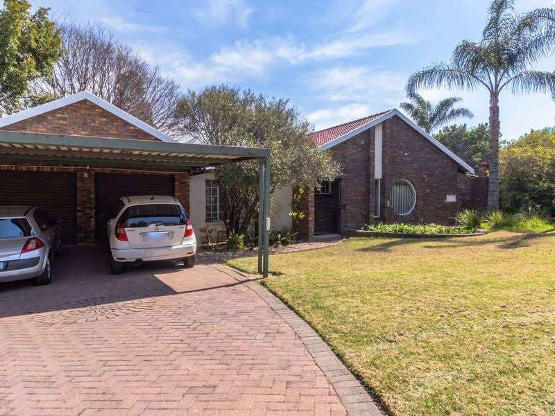 Front view of a brick-faced house featuring a double garage, attached carport, paved driveway, and a well-maintained front garden.