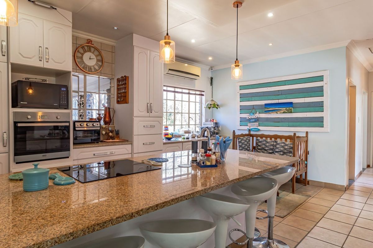 A well-appointed kitchen featuring a large granite island, built-in oven and microwave, electric cooktop, and modern pendant lighting with tiled flooring throughout.