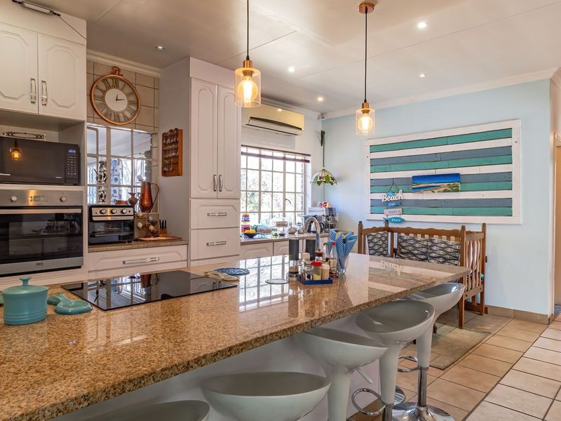A well-appointed kitchen featuring a large granite island, built-in oven and microwave, electric cooktop, and modern pendant lighting with tiled flooring throughout.