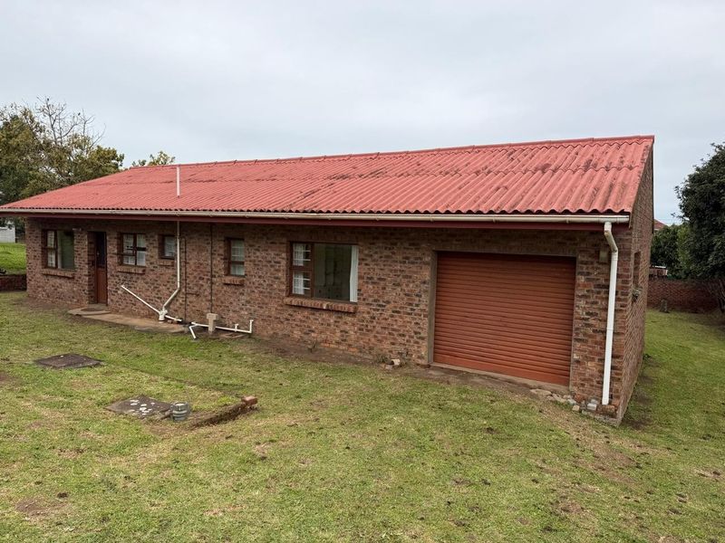 Rear view of a face brick house featuring a corrugated metal roof, integrated roller shutter garage door, and established lawn area.