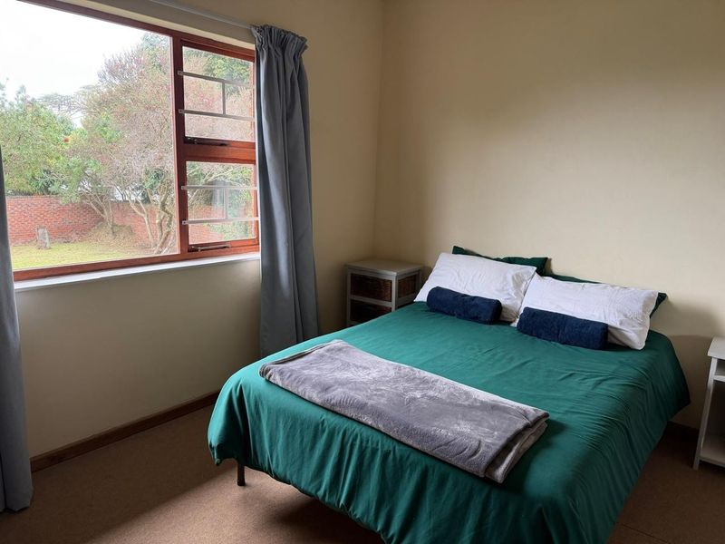 A functional bedroom featuring carpeted flooring and a large window with garden views, providing natural light and a neutral backdrop for personalization.