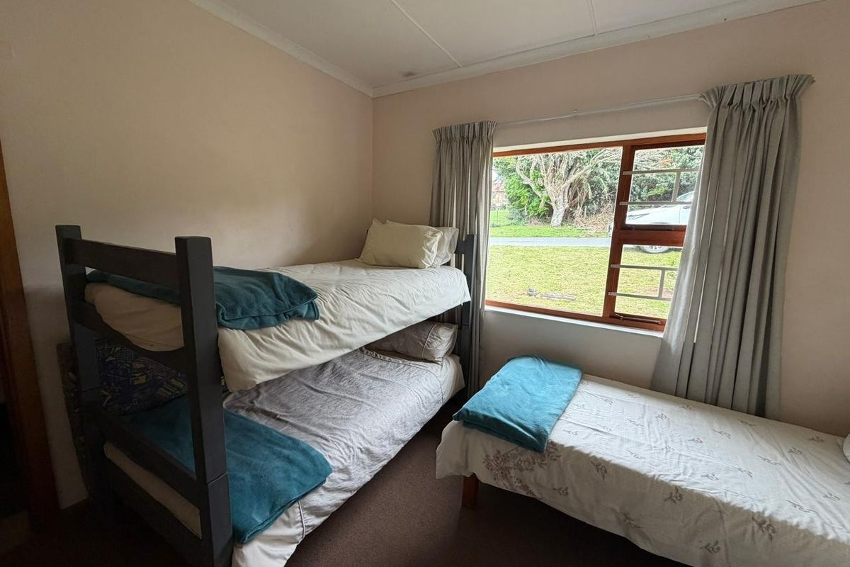 A functional bedroom featuring a large window with security bars and neutral wall finishes, providing natural light and a view of the exterior.