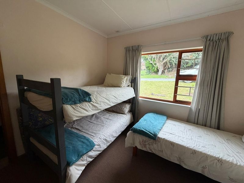 A functional bedroom featuring a large window with security bars and neutral wall finishes, providing natural light and a view of the exterior.