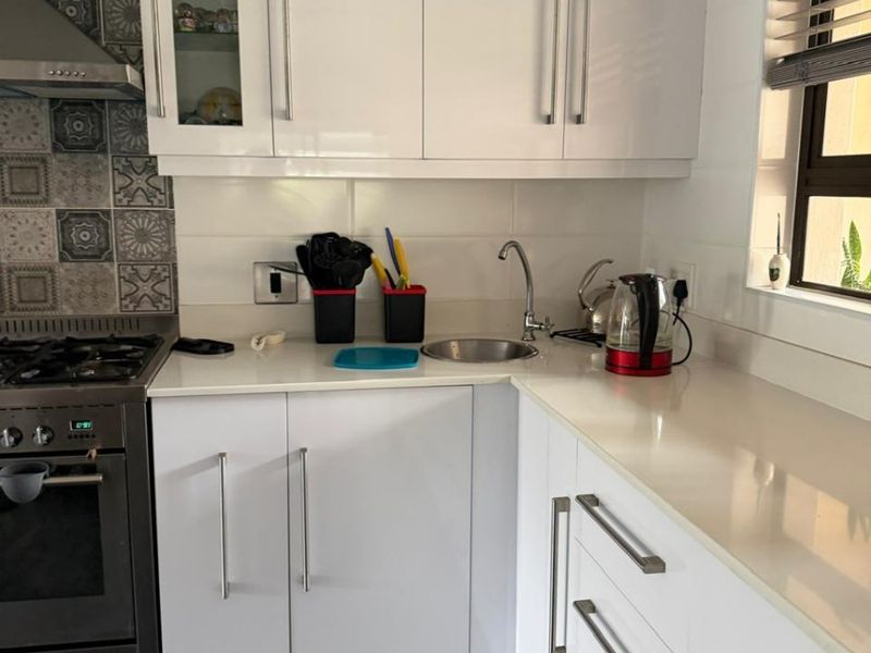 Modern kitchen featuring white high-gloss cabinetry, stone countertops, a gas stove with extractor, and decorative tiled splashback.