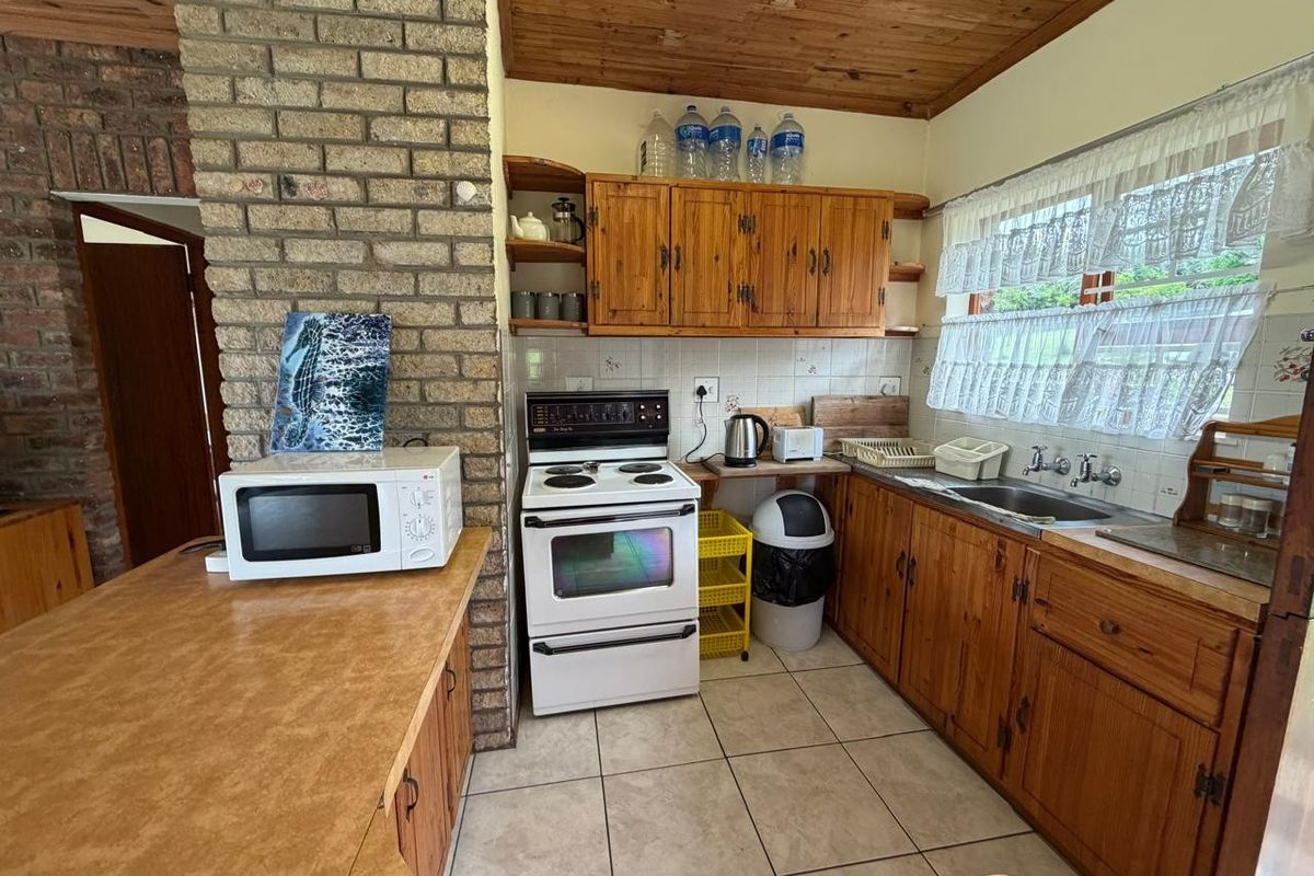 A functional kitchen featuring wooden cabinetry, exposed brickwork, a timber ceiling, and tiled flooring, offering a classic, dated aesthetic ready for modernization.