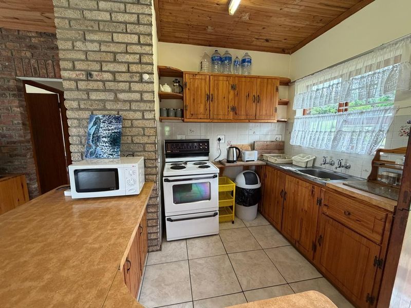 A functional kitchen featuring wooden cabinetry, exposed brickwork, a timber ceiling, and tiled flooring, offering a classic, dated aesthetic ready for modernization.