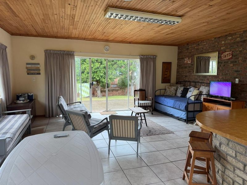 Open plan living area featuring an exposed timber ceiling, brick feature wall, tiled flooring, and sliding glass doors leading to the garden.