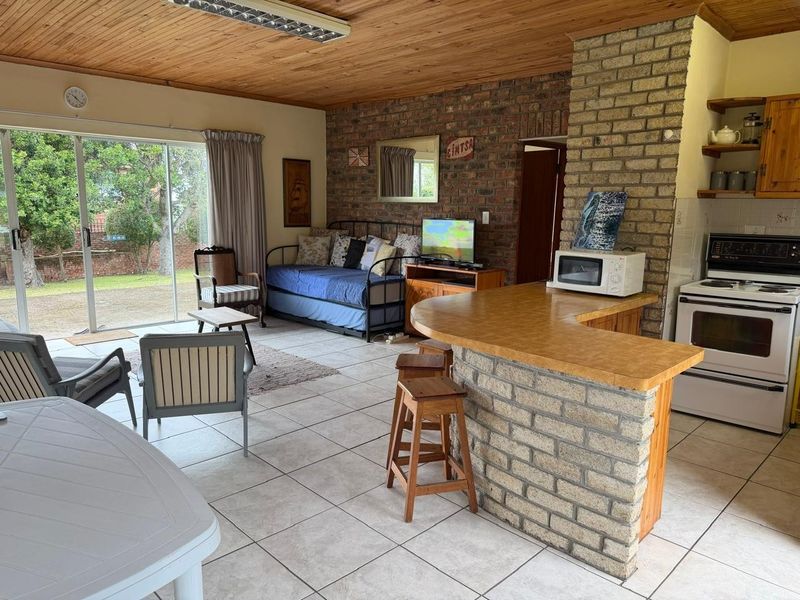 Open-plan living and kitchen area featuring exposed brick walls, timber ceilings, tiled floors, and a breakfast bar with direct access to the garden.