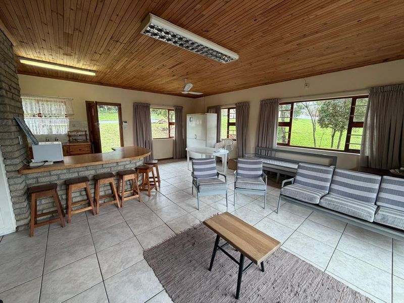 Spacious open-plan living and kitchen area featuring a timber ceiling, tiled floors, and a brick breakfast bar with large windows overlooking the garden.