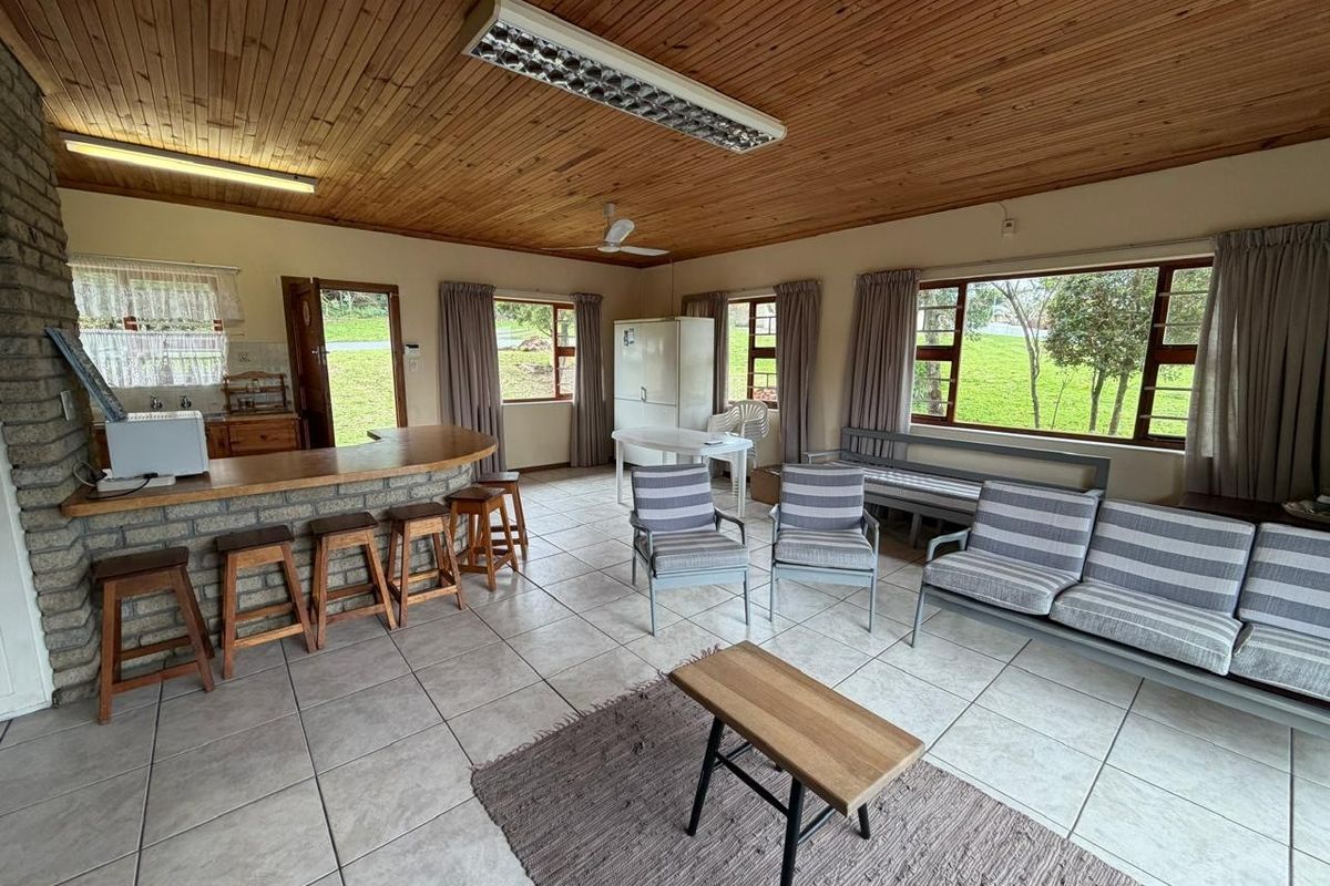 Spacious open-plan living and kitchen area featuring a timber ceiling, tiled floors, and a brick breakfast bar with large windows overlooking the garden.