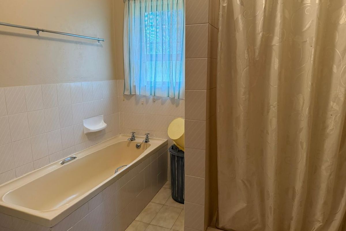 A functional bathroom featuring a built-in bathtub, separate shower enclosure, and neutral ceramic tiling throughout.