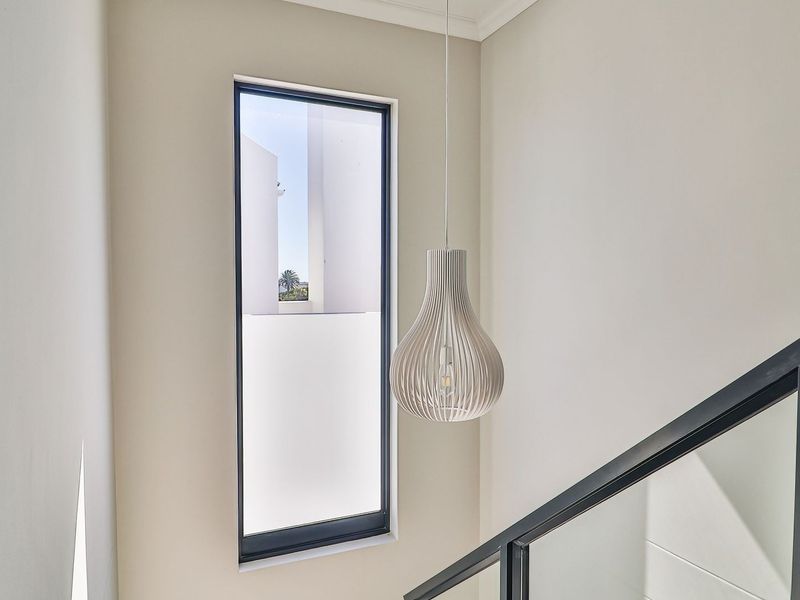 A bright, modern stairwell featuring a sleek glass balustrade, a tall window, and a contemporary pendant light fixture.