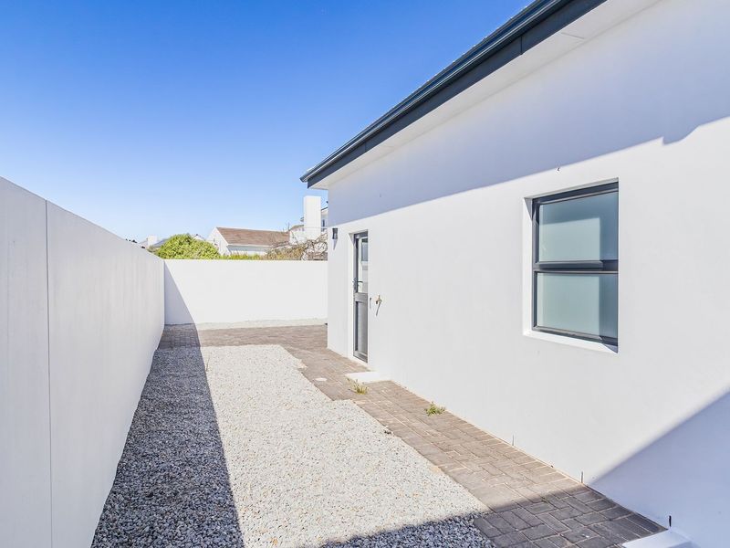 A clean, low-maintenance rear exterior area featuring a paved walkway, gravel landscaping, and high boundary walls for privacy.