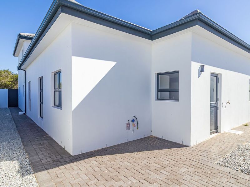 A clean rear exterior view of the property featuring paved walkways, gravel landscaping, and modern aluminium window frames.