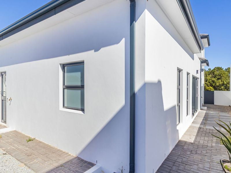 A clean rear exterior view of the property featuring white rendered walls, modern aluminium window frames, and paved pathways.