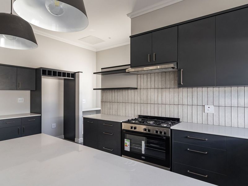Modern kitchen featuring dark cabinetry, white quartz countertops, a gas stove with extractor fan, and a central island with pendant lighting.