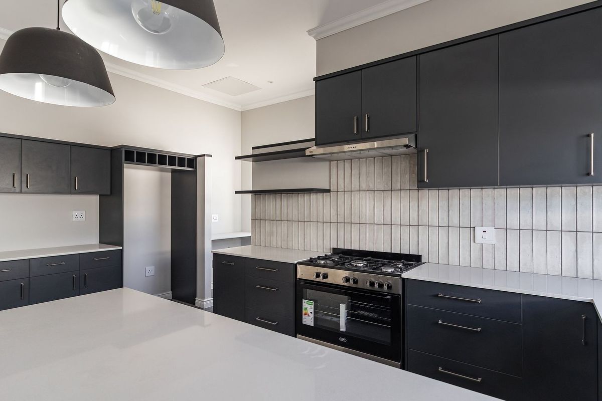 Modern kitchen featuring dark cabinetry, white quartz countertops, a gas stove with extractor fan, and a central island with pendant lighting.