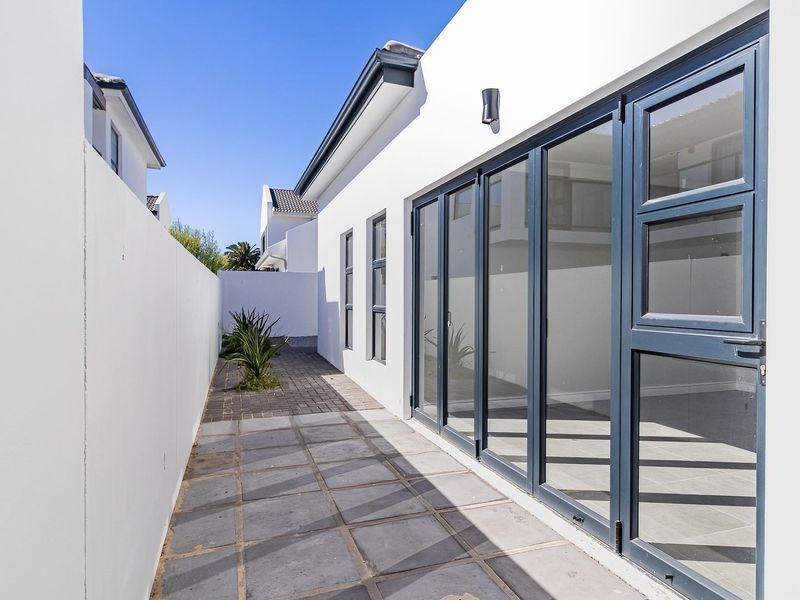 A clean, modern side passage featuring paved flooring, a high boundary wall, and large dark-framed bi-fold doors leading into the home.