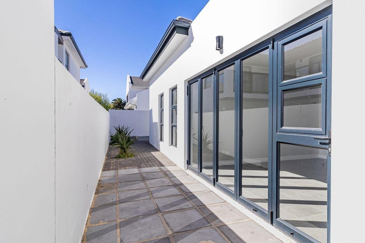 A clean, modern side passage featuring paved flooring, a high boundary wall, and large dark-framed bi-fold doors leading into the home.