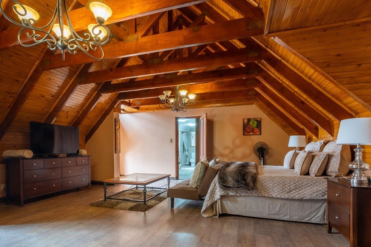 Spacious bedroom featuring vaulted ceilings with exposed timber trusses, warm wood paneling, and laminate flooring, creating a cozy and rustic atmosphere.