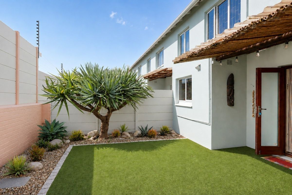 A well-maintained rear courtyard featuring an artificial lawn, landscaped garden beds, a timber pergola, and secure boundary walls with electric fencing.