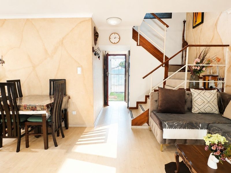 Open-plan living and dining area featuring laminate flooring, a central staircase with wooden handrails, and unique textured wall finishes.