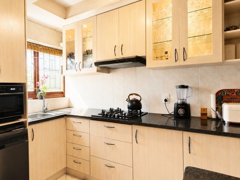 A well-maintained kitchen featuring light-wood cabinetry, black granite countertops, a gas hob, built-in microwave, and integrated glass-fronted display cabinets.