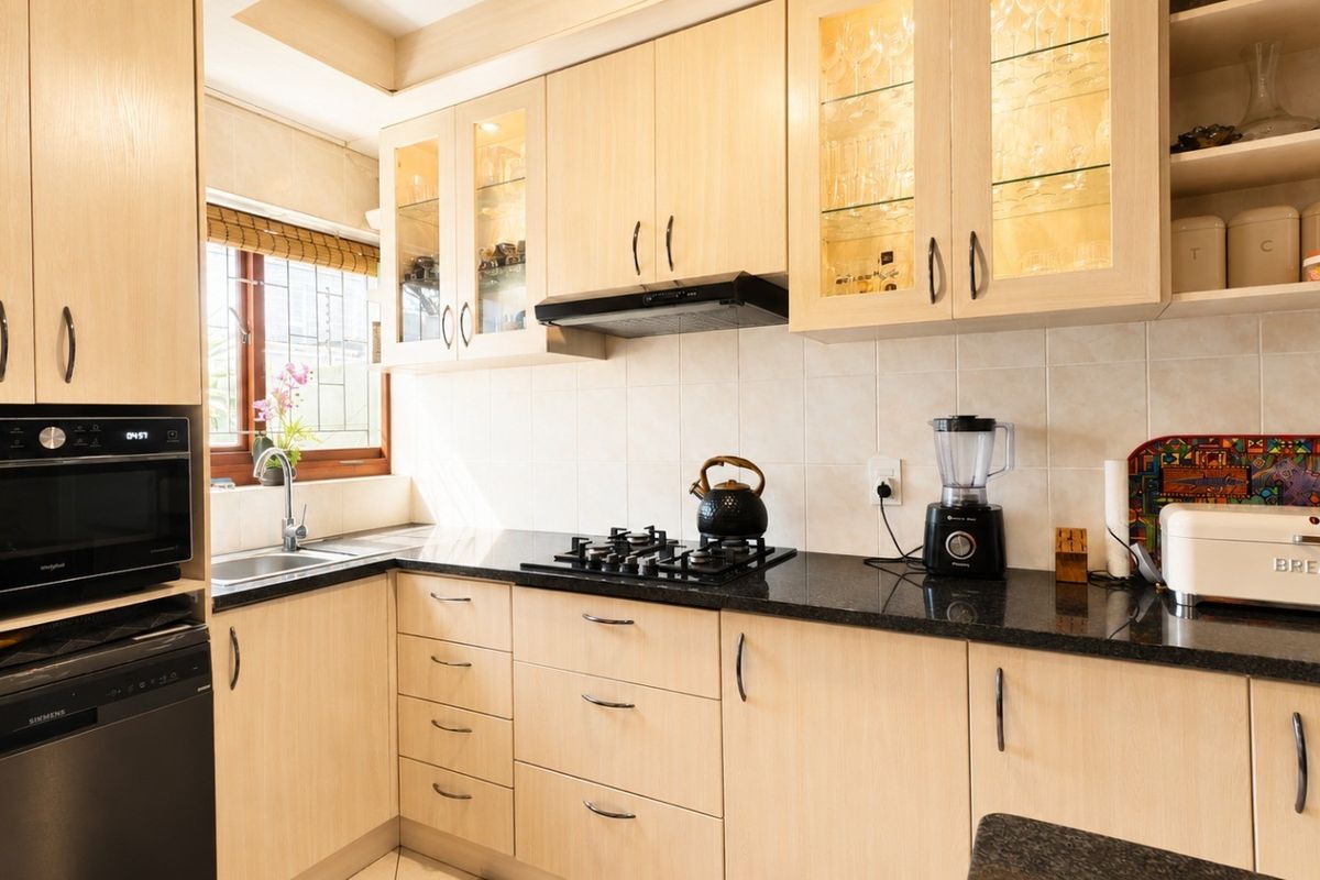 A well-maintained kitchen featuring light-wood cabinetry, black granite countertops, a gas hob, built-in microwave, and integrated glass-fronted display cabinets.