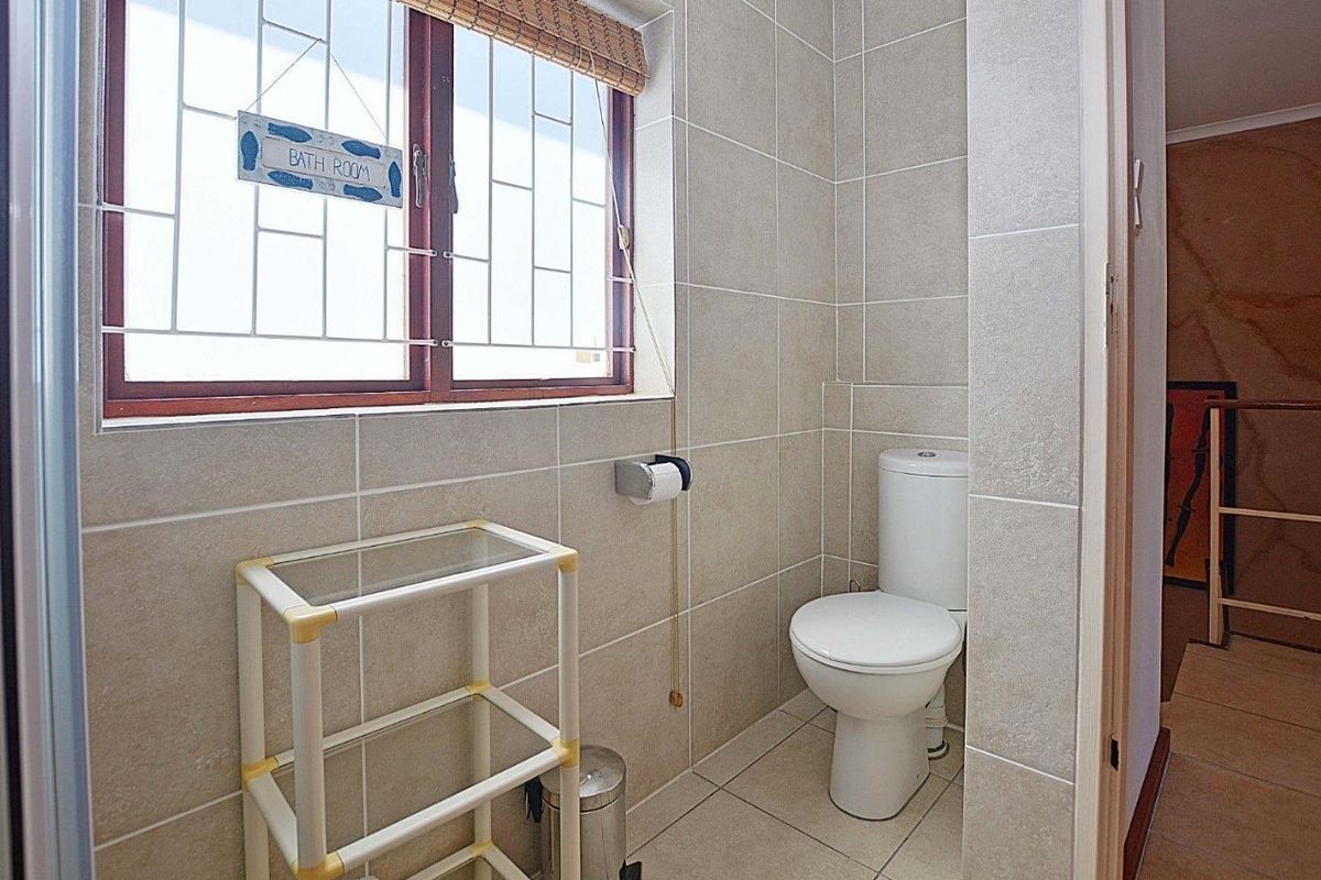 A functional bathroom featuring neutral ceramic wall and floor tiles, a standard toilet, and a window with security bars.