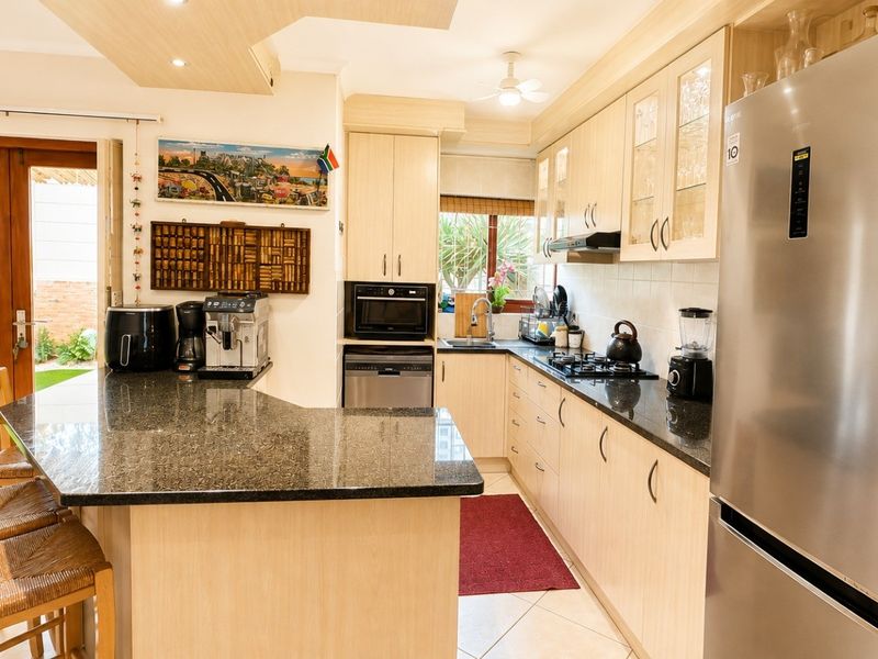 Open-plan kitchen featuring light wood cabinetry, granite countertops, gas hob, and integrated appliances, with direct access to an outdoor patio area.